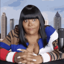 a woman is sitting at a table with her hands folded in front of a microphone and a city skyline in the background .