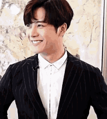 a man in a suit and white shirt is smiling in front of a picture .