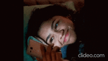 a woman laying on a bed looking at her phone with clideo.com written on the bottom