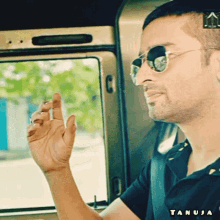 a man wearing sunglasses and a black shirt with tanuja written on the bottom right