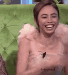 a woman sitting on a green couch laughing with #mayward written on the bottom right