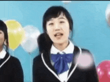 a girl in a school uniform is standing in front of balloons and singing .