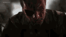 a man with blood on his face is screaming in a dark room .