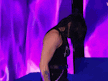 a man in a black tank top is standing in front of a purple and pink background .