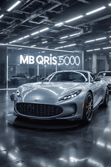 a silver sports car is parked in front of a sign that says mb qris 5000
