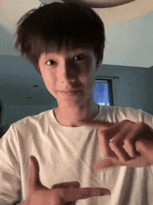 a boy in a white shirt is making a peace sign with his hands