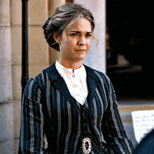 a woman in a striped suit is standing in front of a building and looking at the camera .