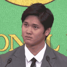 a man in a suit and tie stands in front of two microphones in front of a green background with the letter o on it