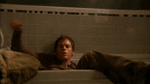 a man in a brown shirt is laying in a bathtub with his legs crossed