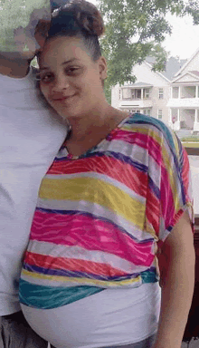 a pregnant woman in a colorful striped shirt is posing for a picture with her husband .