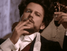a man with a beard is smoking a cigarette and drinking a glass of wine