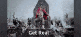 a man in a red jacket is sitting on a throne with the words get real below him