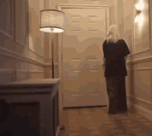 a woman is walking down a hallway towards a door with a lamp .