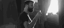 a black and white photo of a man with a beard lighting a match