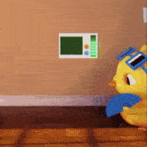 a yellow chicken wearing sunglasses and a fan stands in front of a wall with a thermostat