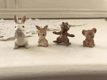 four figurines of animals are lined up on a table including a rabbit a kangaroo and a mouse