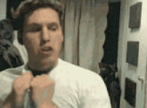 a man in a white shirt is adjusting his tie in front of a mirror in a room .
