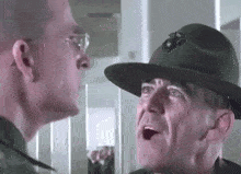 a man in a military uniform and hat is talking to another man in a military uniform and hat .