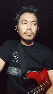 a man wearing a black shirt with the letter u on it is playing a guitar
