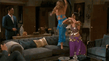 two women are dancing in a living room and one is wearing a blue top