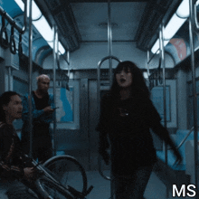 a woman in a black shirt is standing in a dark subway car with the letters ms below her