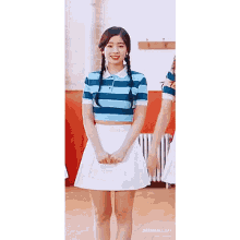 a woman in a striped shirt and a white skirt is standing in a gym with her hands on her hips .