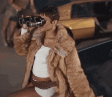 a woman wearing a fur coat and underwear is drinking from a can while looking through binoculars .