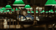 a woman sits at a table in a library with green lamps