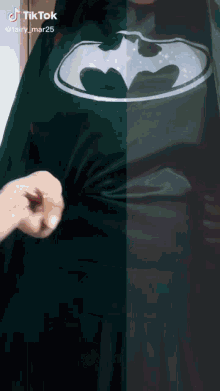a person wearing a green batman shirt is being pinched by another person 's hand .