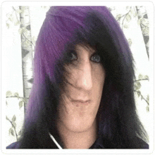 a man with long black and purple hair is standing in front of a white curtain .