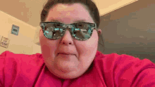 a woman wearing sunglasses and a pink shirt is making a face .