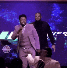 a man in a purple suit is holding a microphone in front of a nissan logo
