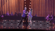 a man and a woman are dancing on a stage with an orchestra in the background