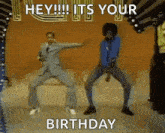 two men are dancing on a stage with the words `` hey !!! it 's your birthday '' written on the bottom .