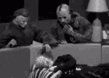 a black and white photo of jason voorhees and freddy krueger sitting on a couch in a living room .