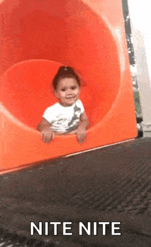 a little girl is sitting on an orange slide with the words nite nite written on the bottom
