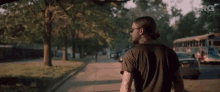 a man with long hair and sunglasses is walking down a street with a bus in the background .