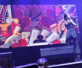 a woman singing into a microphone in front of a large screen with hearts and playing cards