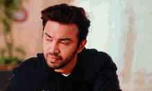 a man with a beard wearing a black sweater looks at the camera