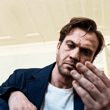 a man with a beard and a white shirt is holding his hand to his face