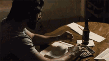 a man is using a calculator while sitting at a table with a bottle of beer