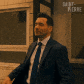 a man in a suit and tie is standing in front of a window with saint pierre written on it