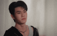 a young man wearing a necklace and earrings is looking at something .