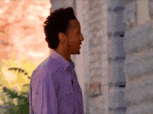 a man in a purple shirt stands in front of a stone wall