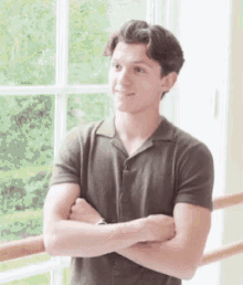 a young man in a green shirt is standing with his arms crossed in front of a window .