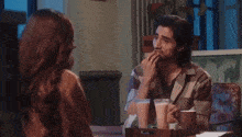 a man and a woman are sitting at a table with drinks and talking to each other .