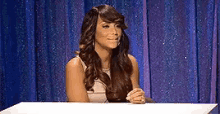 a woman with long hair is sitting at a table in front of a blue curtain .