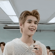 a young man in a white sweater is smiling in a room