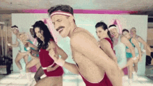 a group of people are dancing in a gym while a man is dancing without a shirt on .