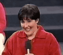 a woman in a red jacket is holding a microphone and smiling
